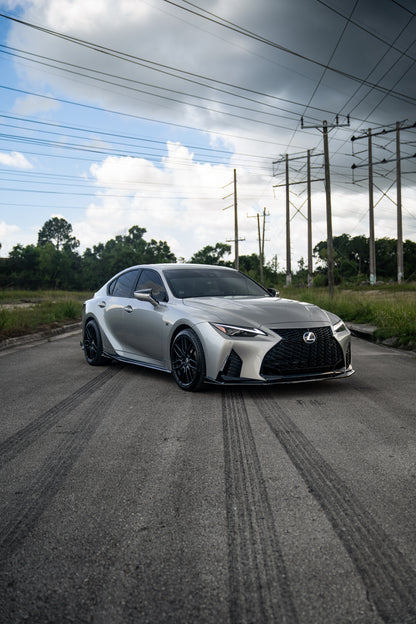 A silver Lexus is500 nia splitter lip body kit sedan parked on an asphalt road outdoors, with power lines, trees, and a cloudy sky in the background.